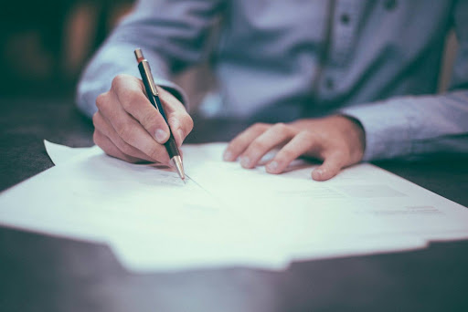Two business professionals reviewing and signing deal documents during a private equity acquisition, representing the point in an M&A transaction where hazmat liability transfers from seller to buyer.